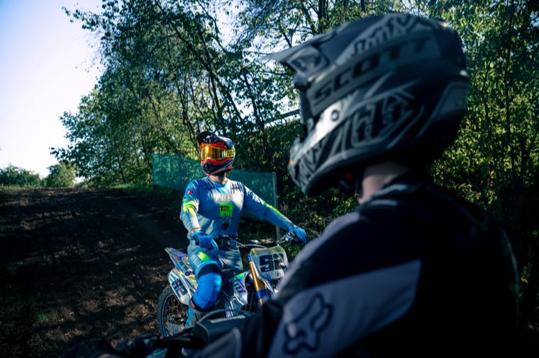 Deux pilotes de motocross à l'arrêt sur un chemin en forêt.